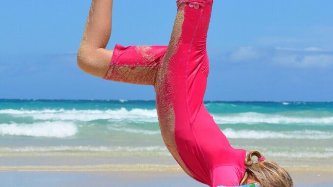 turnendes Mädchen am Strand in UV-Schutzkleidung